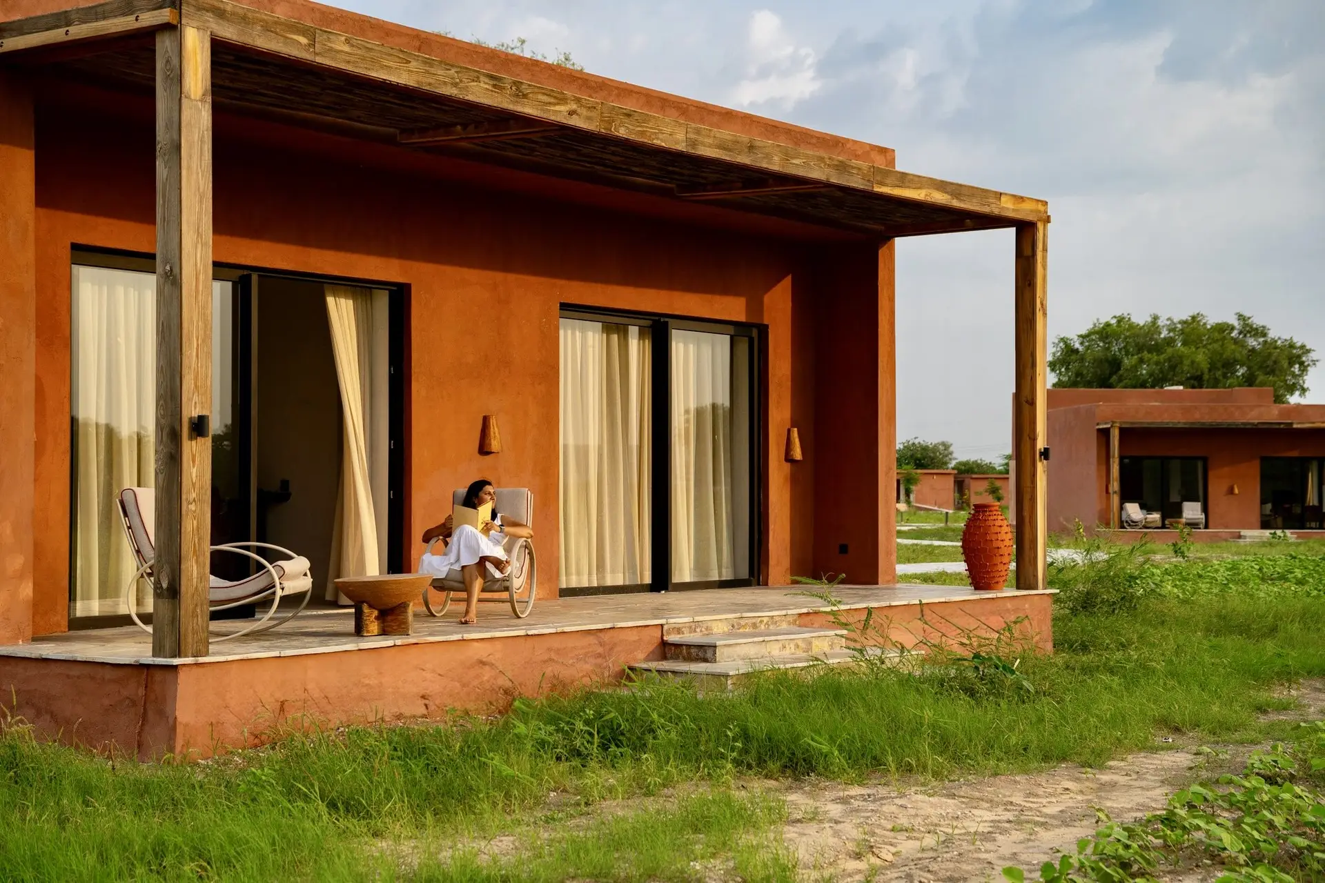 A guest reading on the private veranda of a terracotta villa, farm fields beyond at golden hour