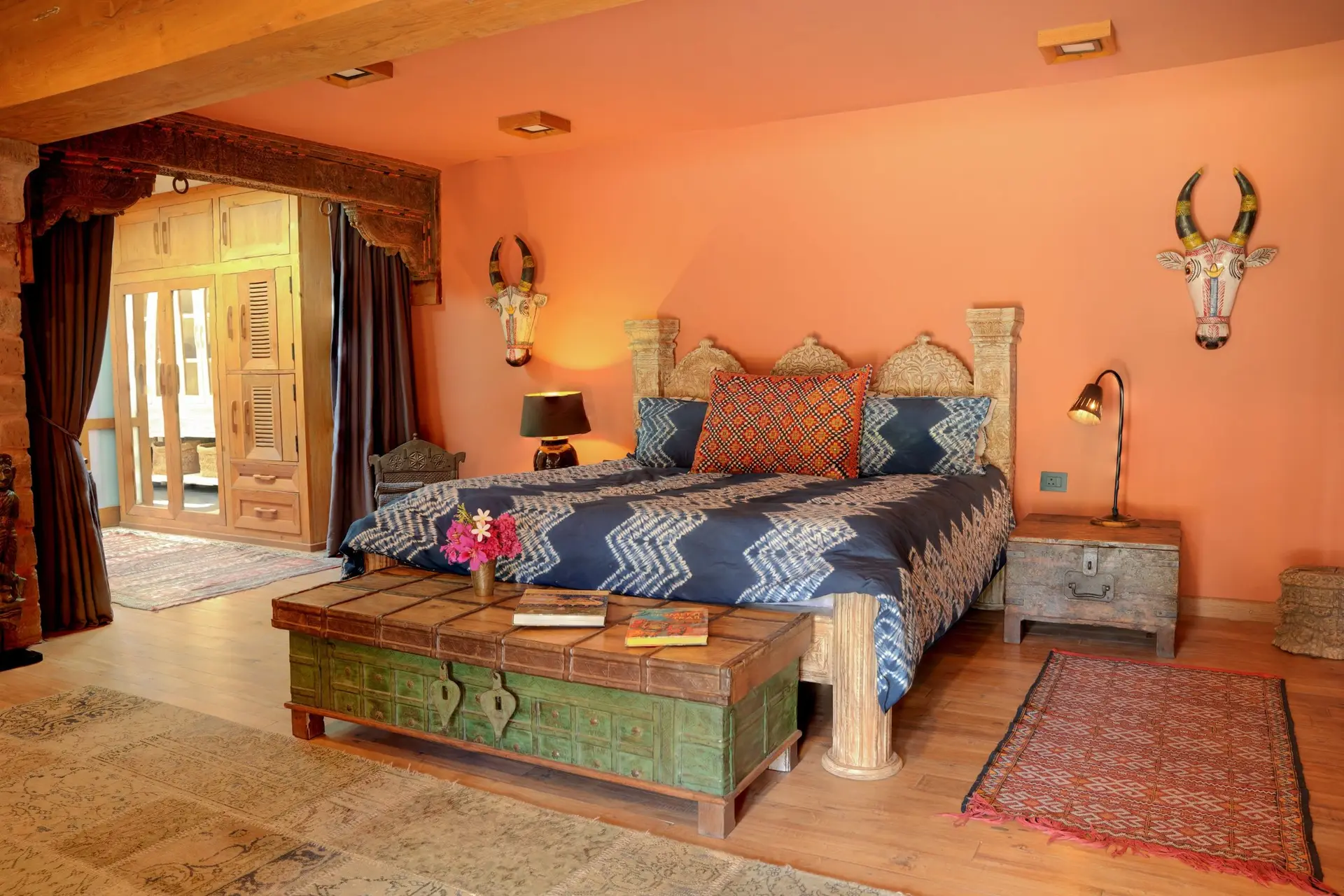 A heritage suite with coral walls, a carved headboard, indigo ikat bedding and painted Rajasthani cow masks