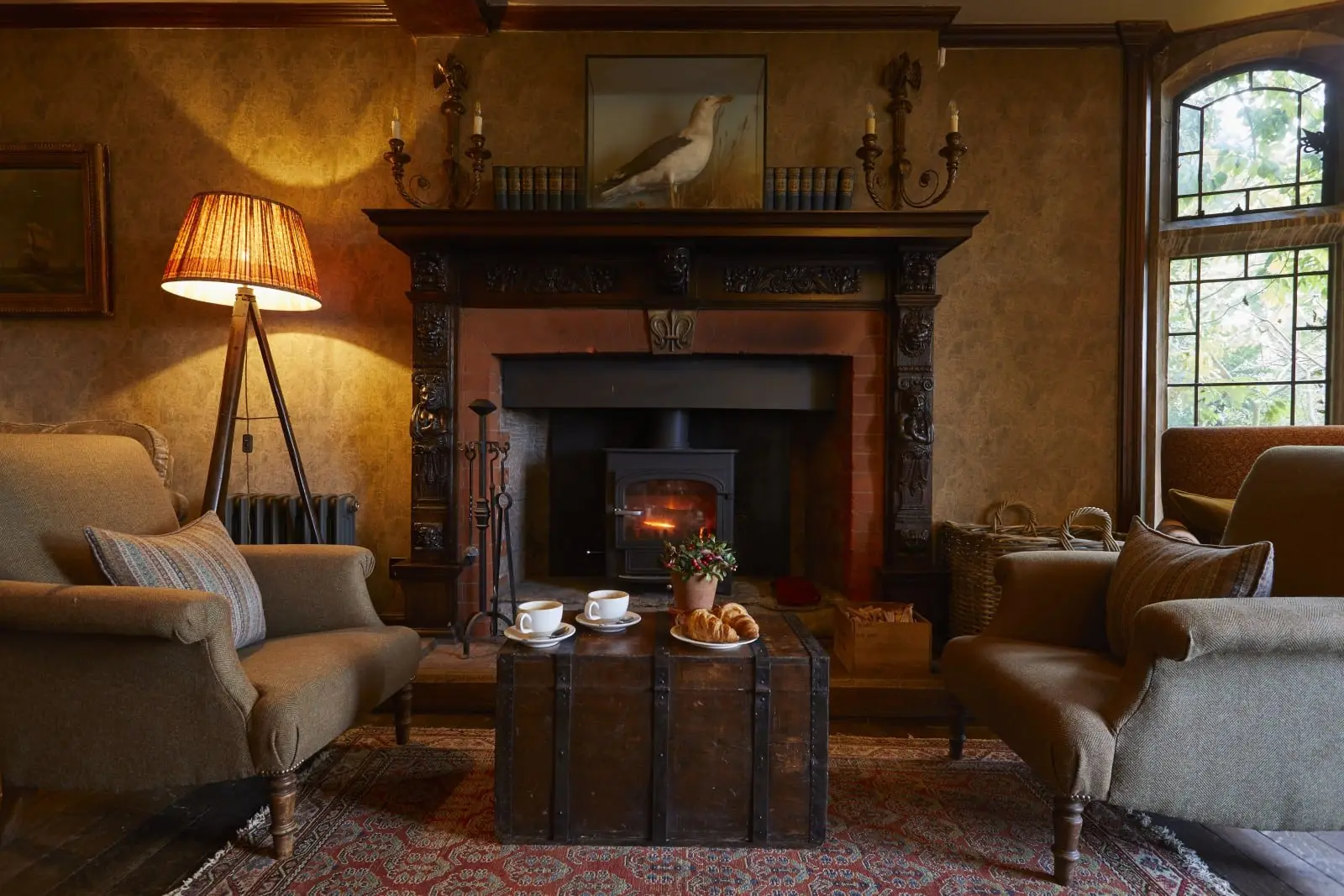 A snug sitting room with a lit wood burner, carved fireplace and tweed armchairs